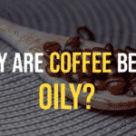 - Oily coffee beans on a wooden spoon. Written Text “Why are Coffee Beans Oily?”