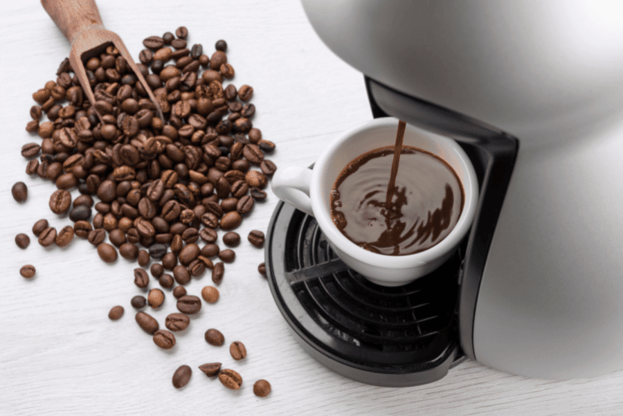 Coffee being poured out of a coffee maker with coffee beans on a white background